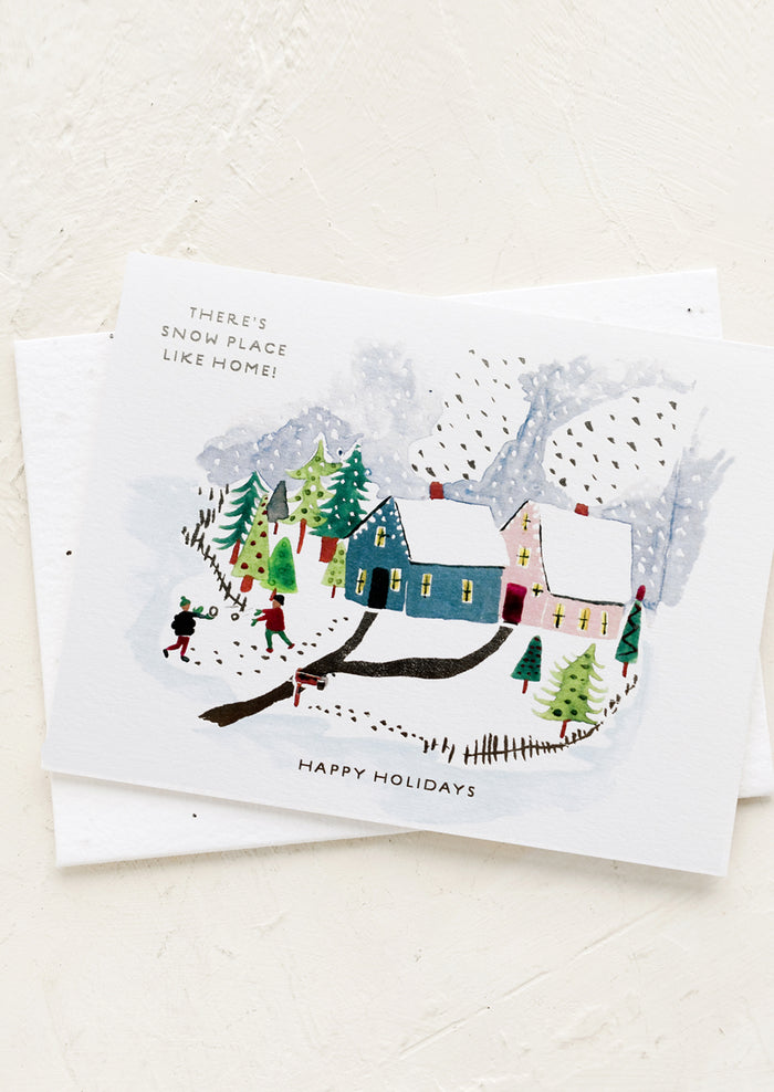 A greeting card with snowy village illustration, text reads "There's Snow Place Like Home!".