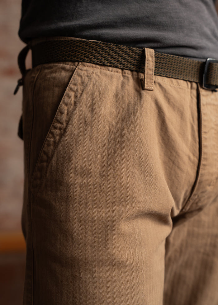 Close-up of a person wearing brown pants with a black belt, highlighting the fabric texture and stitching details.