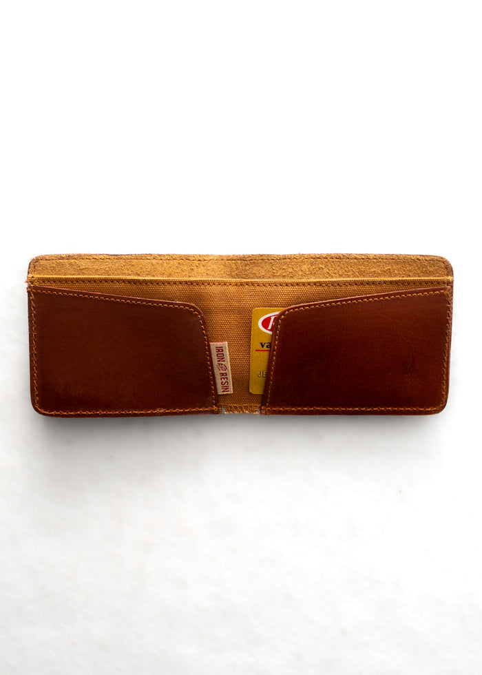 Open brown leather wallet with two visible card slots, holding a yellow card. The wallet is placed on a white background.