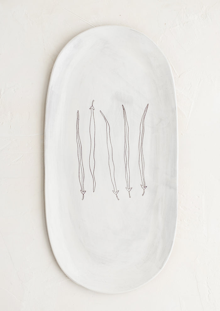 An oval shaped ceramic serving platter with hand drawn green beans illustration at center.